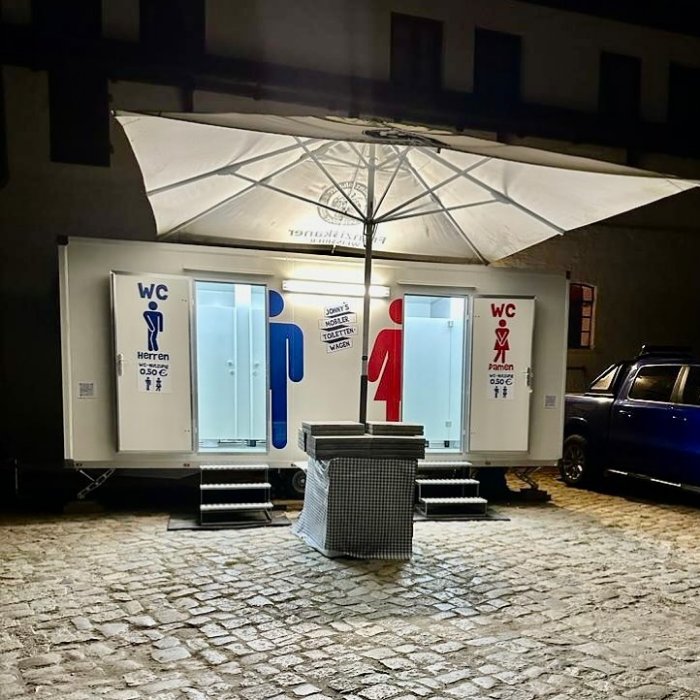 Beleuchteter Toilettenwagen bei Nacht mit Stehtisch